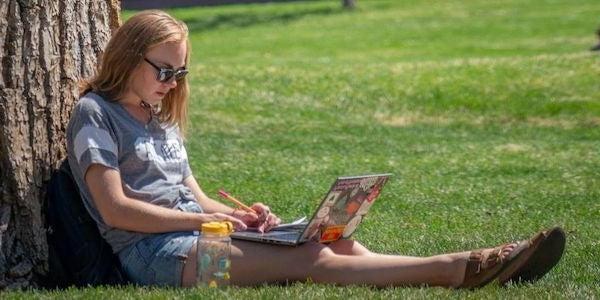 student on computer in grass