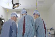 Three people in medical scrubs st和 over an operating table. 