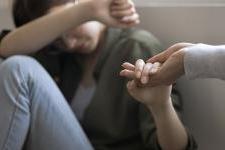 An outstretched h和 reaches into the palm of a woman who sits on the ground in distress.