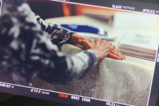 An image of a film camera screen showing an elderly woman's crossed hands.